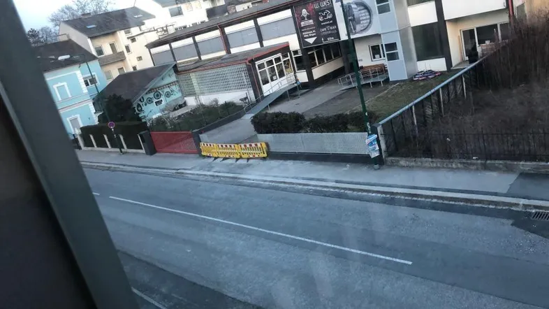 Blick von der Straße auf Gebäude mit Geschäften und gelben Absperrungen in einer städtischen Umgebung.
