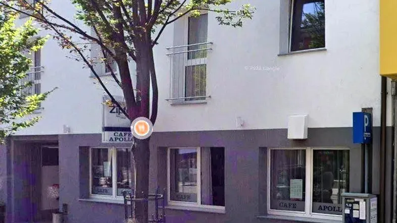 Gebäudefassade mit einem Café im Erdgeschoss und einer zweifarbigen Gestaltung in Weiß und Grau in urbaner Umgebung.