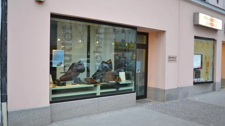 Fassade eines Geschäftsgebäudes mit großem Schaufenster, das Herrenschuhe präsentiert.