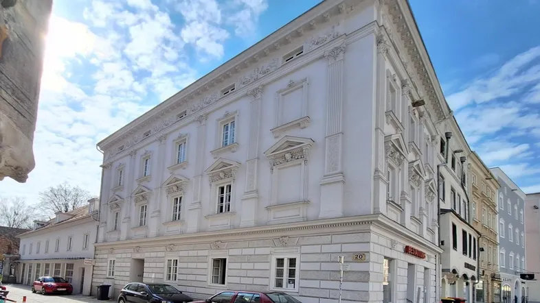 Historisches Eckgebäude mit aufwendiger Fassadengestaltung und gepflasterter Straße davor unter blauem Himmel.