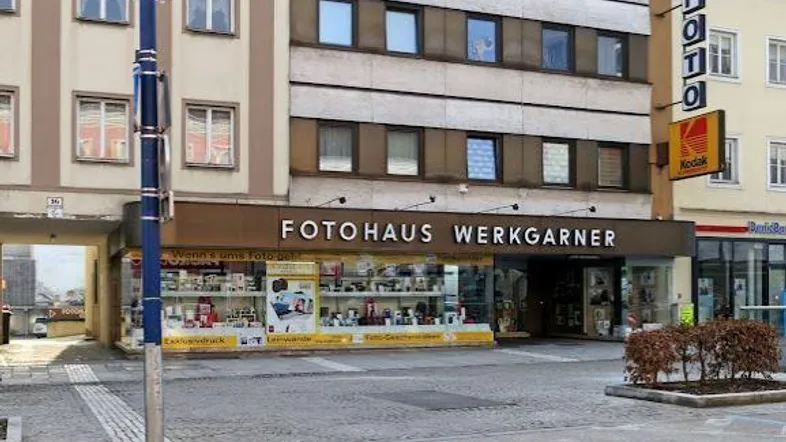 Gebäudeansicht eines Geschäftshauses mit großen Schaufenstern und Werbeschildern an einer belebten Straße.