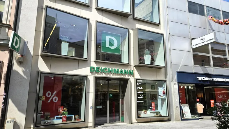 Fassade eines Geschäftsgebäudes mit großen Schaufenstern und dem Deichmann-Logo in einer belebten Einkaufsstraße.