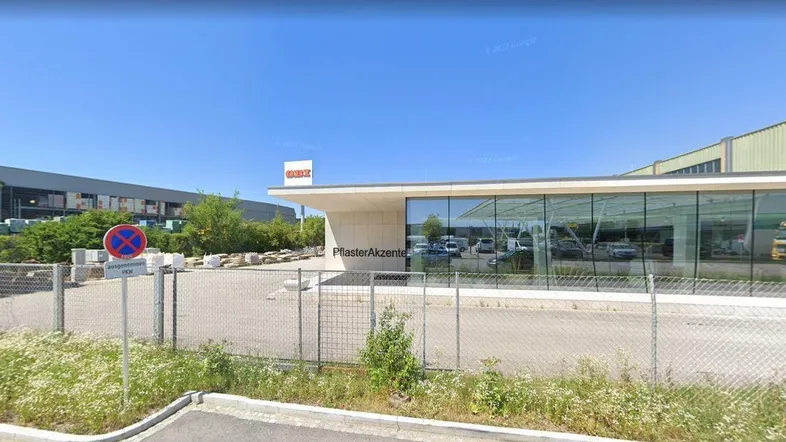 Moderne Gewerbeimmobilie mit großer Glasfassade und Parkplätzen unter blauem Himmel.