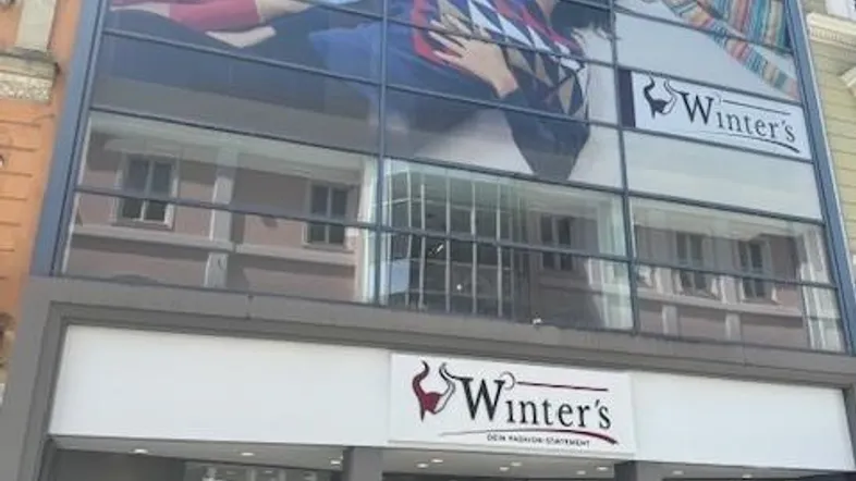 Fassade eines Geschäftsgebäudes mit großer Glasfront und Werbebanner, das Menschen zeigt.
