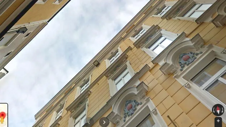 Ansicht einer historischen gelben Gebäudefassade mit verzierten Fenstern und architektonischen Details unter bewölktem Himmel.