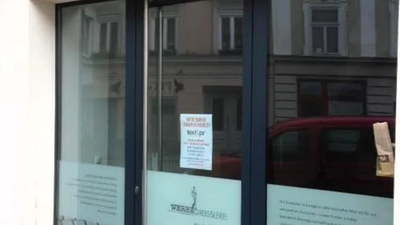 Eingangsbereich eines Geschäfts mit großer Glasfront und reflektierenden Fenstern, die die Straße zeigen.