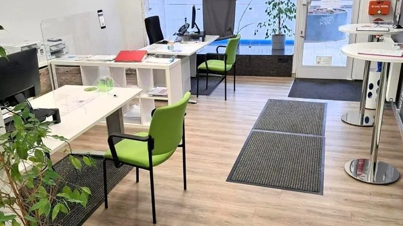 Heller Büroraum mit mehreren Arbeitsplätzen, großen Fenstern zur Straße und modernem Laminatboden.