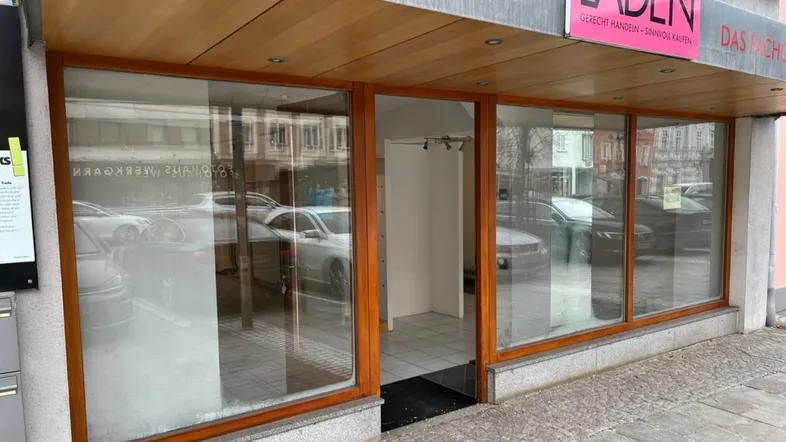 Leere Ladenfassade mit großen Schaufenstern und Holzelementen, die auf eine Vermietung warten.