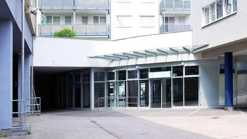 Eingangsbereich eines modernen Gebäudes mit großen Glasfronten und darüberliegenden Wohnbalkonen.