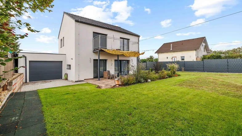 Modernes Einfamilienhaus mit großem Garten, Terrasse und Balkon, umgeben von viel Grün.