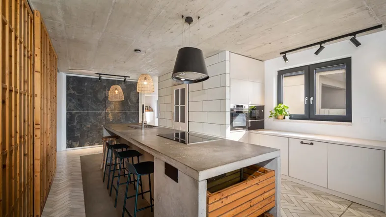 Moderne offene Küche mit Betoninsel, Holzelementen und freiliegender Betondecke.