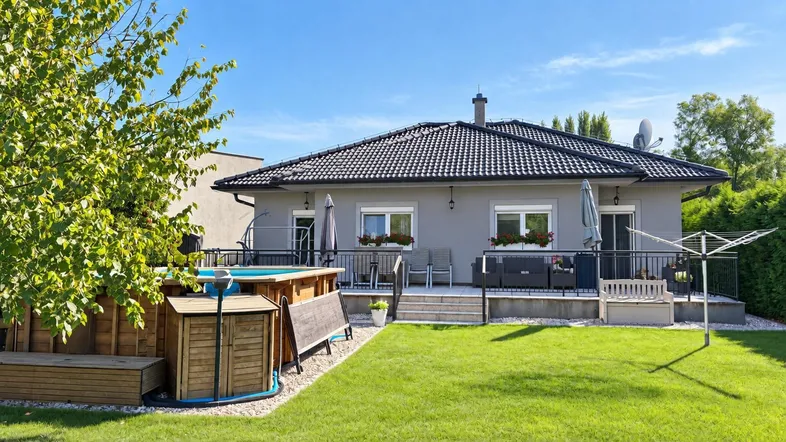 Hausrückseite mit Garten, Pool und Terrasse unter blauem Himmel.