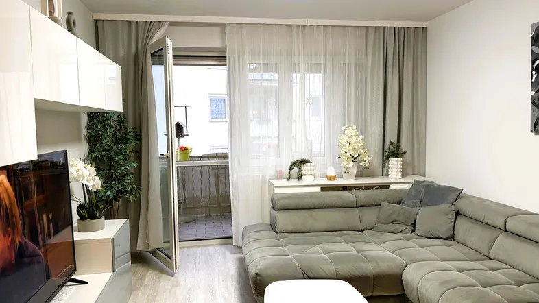 Helles Wohnzimmer mit gemütlichem Ecksofa, modernen Möbeln und direktem Zugang zum Balkon.