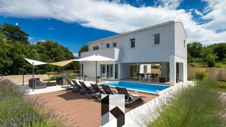 Moderne Villa mit Pool, Holzterrasse und Liegestühlen unter blauem Himmel.