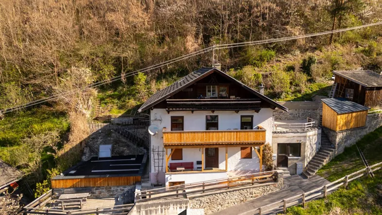 Traditionelles Haus in Hanglage mit Holzbalkon und umgebender Natur, umgeben von Bäumen.