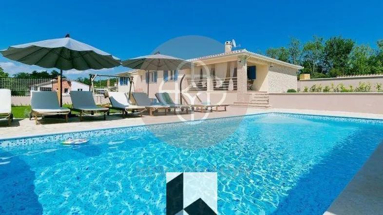Großer Poolbereich mit Sonnenliegen und Blick auf die moderne Villa unter blauem Himmel.