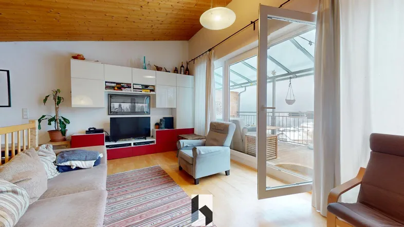 Helles Wohnzimmer mit Holzbalkendecke, Parkettboden und Zugang zu einem verglasten Balkon.