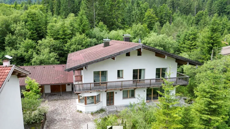 Großzügiges Einfamilienhaus in alpiner Umgebung, umgeben von dichtem Wald und Bergen.