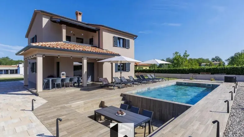 Modernes Haus mit großem Poolbereich, Sonnenliegen und Essbereich im Freien unter blauem Himmel.