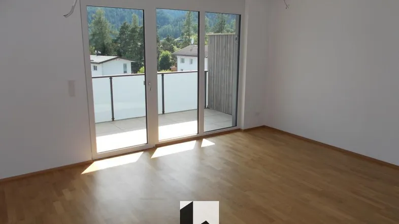 Helles Zimmer mit Holzboden, großen Fenstern und Zugang zu einem Balkon mit Bergblick.