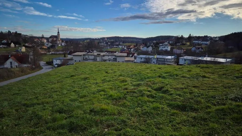 Weitläufige Grünfläche mit Blick auf ein charmantes Dorf und eine Kirche im Hintergrund unter blauem Himmel.