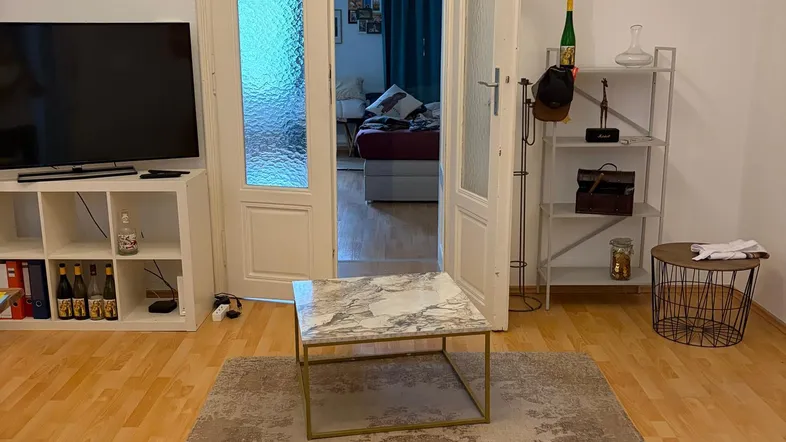 Helles Wohnzimmer mit Parkettboden, modernem Teppich und Doppeltüren zu einem weiteren Raum.