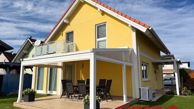 Modernes Einfamilienhaus mit gelber Fassade, überdachter Terrasse und Gartenbereich.