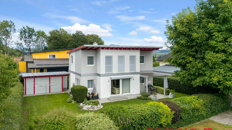 Modernes Einfamilienhaus mit gepflegtem Garten, Terrasse und Gartenhaus unter blauem Himmel.