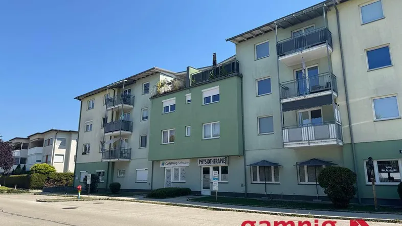 Gebäudeansicht mit mehreren Balkonen und Geschäften im Erdgeschoss unter blauem Himmel.