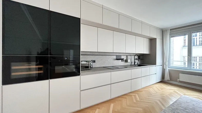 Moderne Einbauküche mit hellen Fronten, integrierten Geräten und Fischgrätparkettboden.
