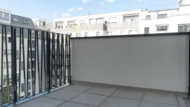 Geräumiger Balkon mit modernem Geländer und Blick auf umliegende Gebäude unter blauem Himmel.