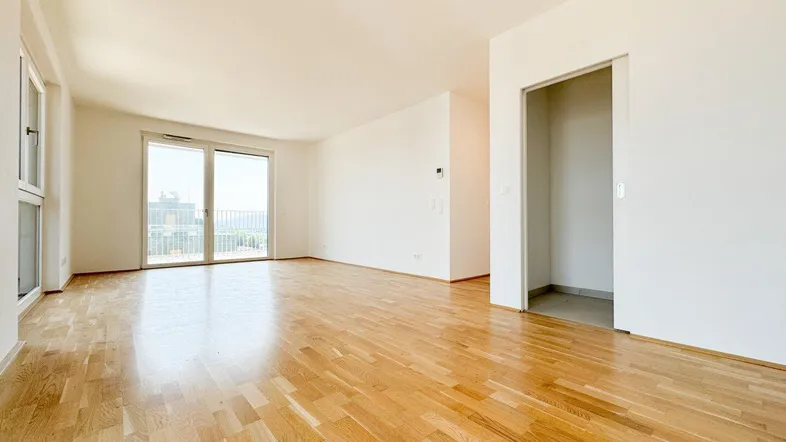 Helles Wohnzimmer mit Parkettboden, großen Fenstern und Zugang zum Balkon.