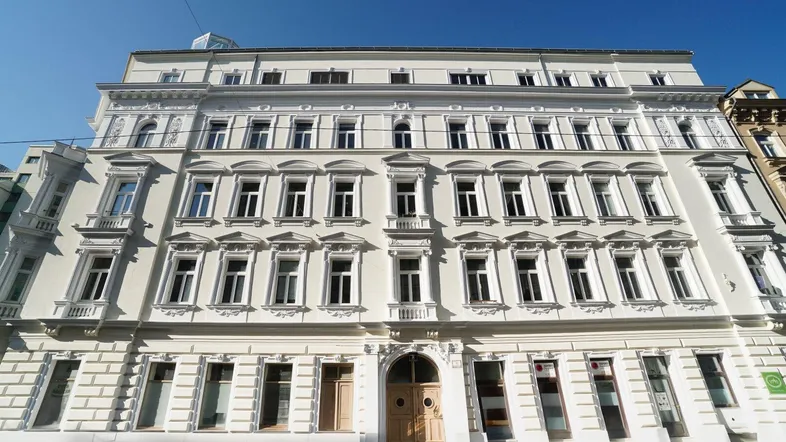 Historische Fassade eines Mehrfamilienhauses mit vielen Fenstern und klassischer Architektur.