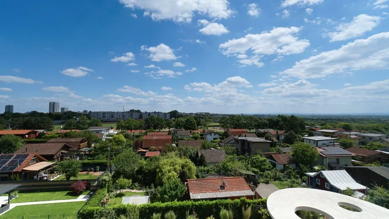 Weitläufiger Blick über eine grüne Wohnsiedlung mit vielen Häusern unter blauem Himmel.