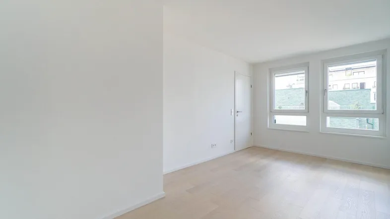 Helles, leeres Zimmer mit hellem Parkettboden und zwei großen Fenstern, bereit zur Einrichtung.