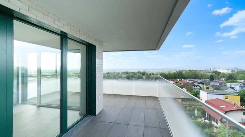 Geräumiger Balkon mit Glasgeländer und weitem Blick über die Stadt und die umliegende Landschaft.