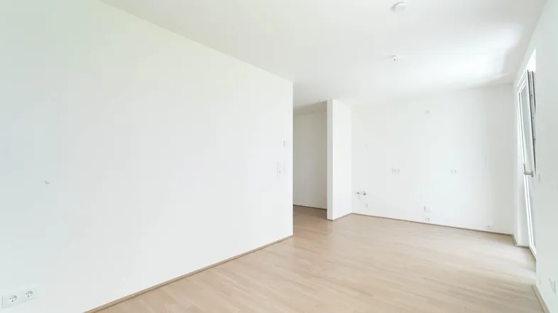 Helles, leeres Zimmer mit Parkettboden und weißen Wänden, bereit zur individuellen Gestaltung.