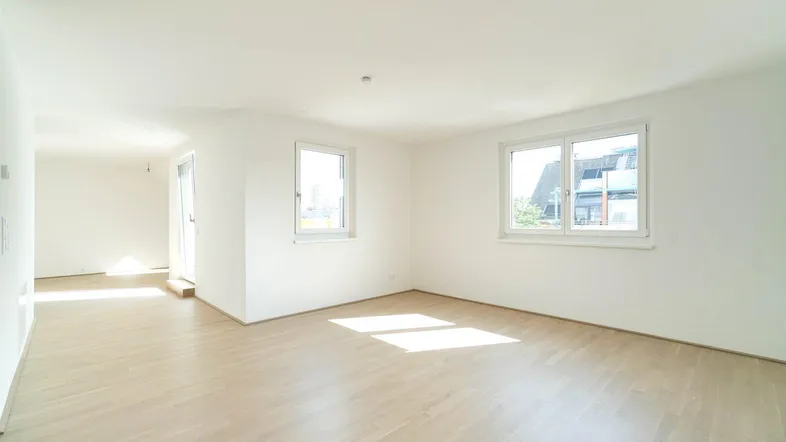 Helles, leeres Zimmer mit hellem Parkettboden und großen Fenstern, das viel Tageslicht hereinlässt.