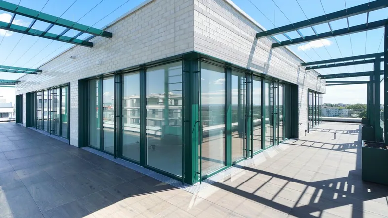 Große Dachterrasse eines modernen Gebäudes mit raumhohen Fenstern und grünen Akzenten.