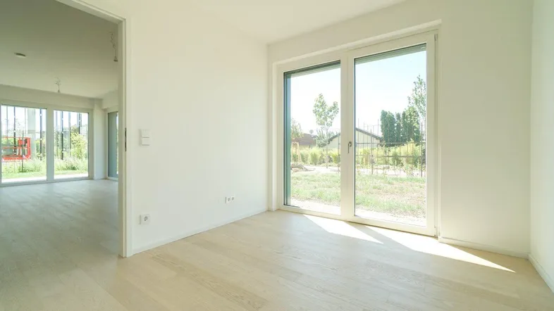 Helles Zimmer mit großen Fenstern und hellem Parkettboden, bietet Zugang zum Außenbereich.