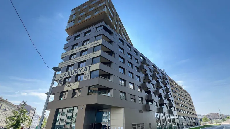 Modernes Wohngebäude mit markanter Architektur und vielen Balkonen unter blauem Himmel.