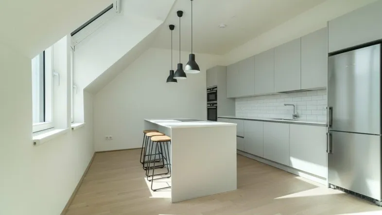 Moderne Küche in Dachgeschosswohnung mit Kücheninsel, hellgrauen Schränken und viel Tageslicht durch Dachfenster.