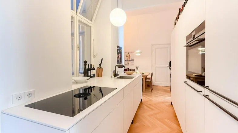 Moderne weiße Küche mit Induktionskochfeld, Backofen, Spülbecken und hellem Fischgrätparkettboden.