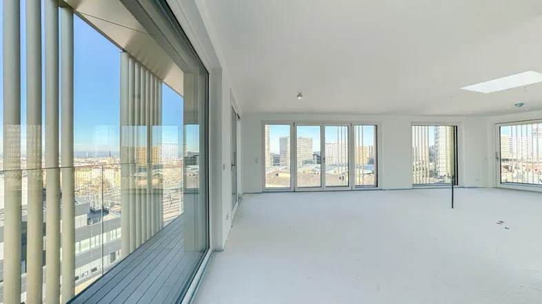 Heller, unmöblierter Wohnraum mit großen Fenstern, die einen weiten Stadtblick und Zugang zum Balkon bieten.