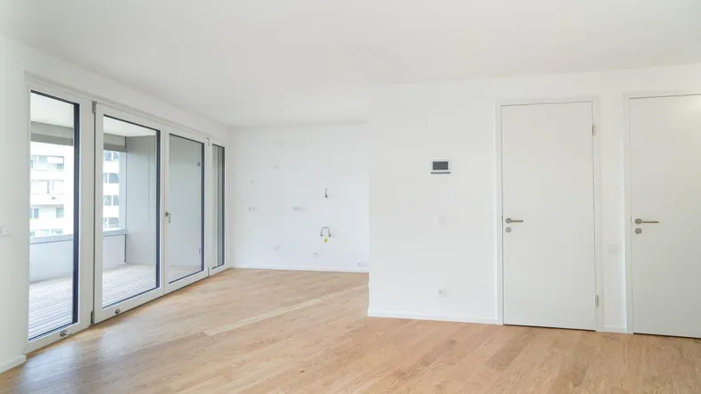 Helles, leeres Zimmer mit Parkettboden und großen Glasfronten zum Balkon, bereit zum Einzug.