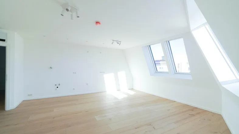 Helles, unmöbliertes Zimmer im Dachgeschoss mit Holzboden und schrägen Fenstern.