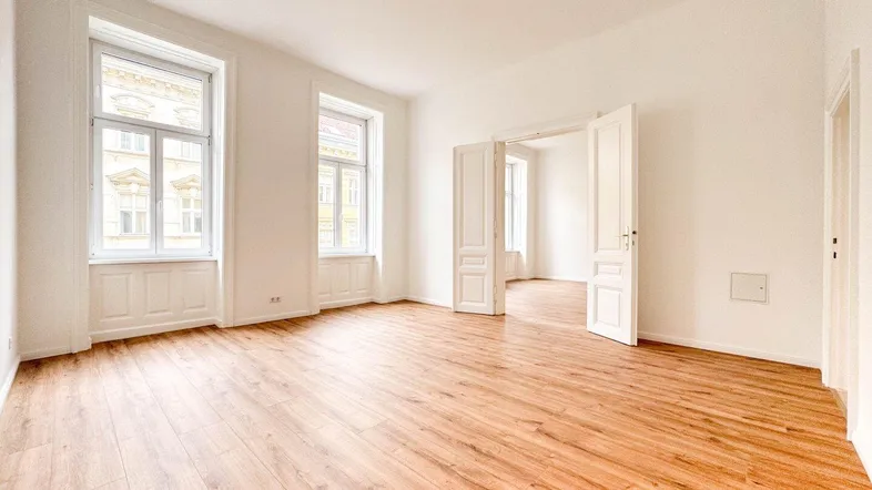 Helles Wohnzimmer mit Holzboden und hohen Fenstern, das viel Tageslicht hereinlässt und frisch renoviert wurde.