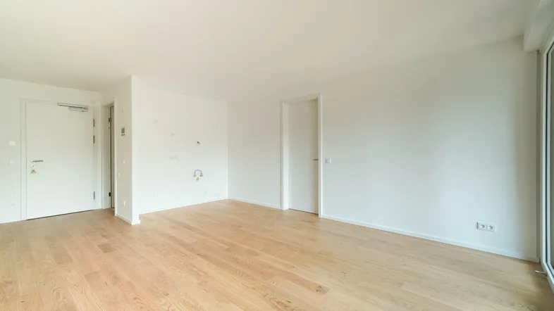 Helles, leeres Wohnzimmer mit hellem Parkettboden und weißen Wänden, bereit zur individuellen Gestaltung.