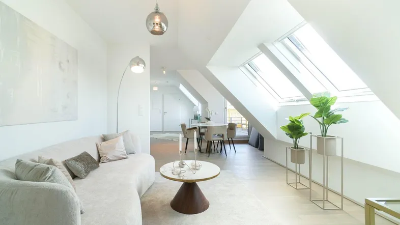 Helles Dachgeschoss-Wohnzimmer mit Schrägdachfenstern, modernem Sofa und Essbereich.