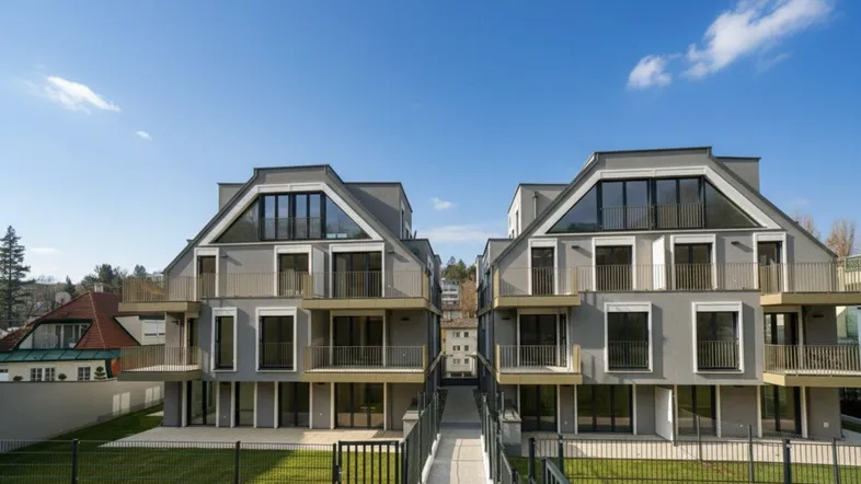 Zwei moderne Mehrfamilienhäuser mit Balkonen, großen Fenstern und gepflegten Grünflächen unter blauem Himmel.